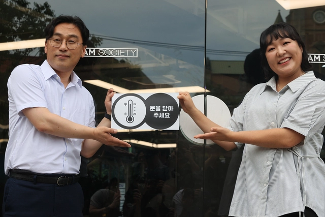 이원주(왼쪽) 산업통상자원부 대변인과 개그우먼 이수지 씨가 2일 서울 중구 명동 온드림소사이어티에서 열린 2025년도 여름철 에너지 절약 캠페인 출범식에서 매장 정문에 에너지 절약을 당부하는 온도주의 스티커를 부착하고 있다. 연합뉴스