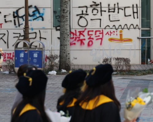 지난 2월 동덕여대 캠퍼스에서 열린 학위수여식에서 졸업생들이 래커칠 낙서로 얼룩진 벽 앞을 지나가고 있다. 연합뉴스