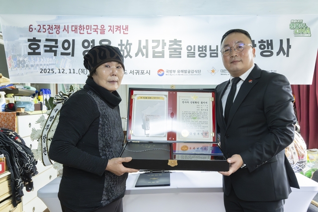 고 서갑출 일병의 며느리인 이정순(72· 왼쪽)씨와 조해학(육군 중령·오른쪽) 국방부유해발굴감식단장 직무대리가 11일 제주 서귀포에 거주하는 고인의 며느리 이정순씨 자택에서 열린 호국영웅 귀환행사에서 호국의 얼 함을 들고 기념사진을 촬영하고 있다.국방부 제공