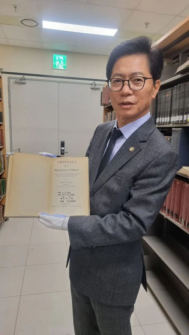 황정근 국회도서관장이 시드니 디치온의 저서 ‘민주적 문화의 무기고’를 들어 보이고 있다. 책 안쪽에는 ‘미국 공보원 대여’ 고무도장이 찍혀 있다.  국회도서관 제공