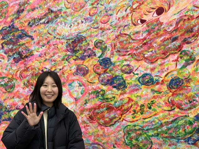아야코 록카쿠 작가가 토탈미술관에 전시된 자신의 작품 앞에서 손을 들고 웃고 있다.