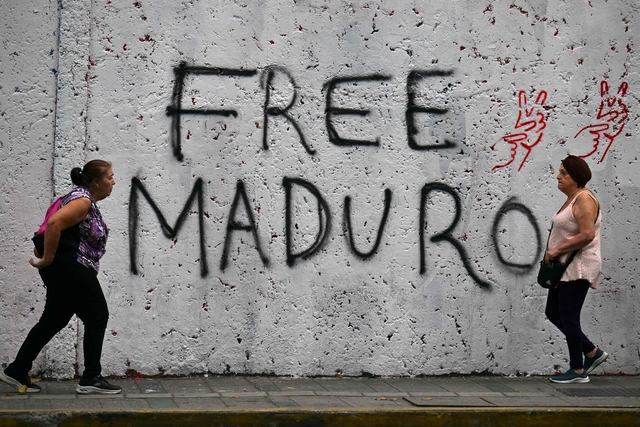 10일 베네수엘라 카라카스에서 시민 두 명이 마약 및 무기 혐의로 재판을 받기 위해 지난 3일 뉴욕으로 납치돼 연행된 베네수엘라의 축출된 대통령 니콜라스 마두로와 그의 부인 실리아 플로레스의 석방을 요구하는 그래피티 앞을 지나가고 있다. AFP 연합뉴스