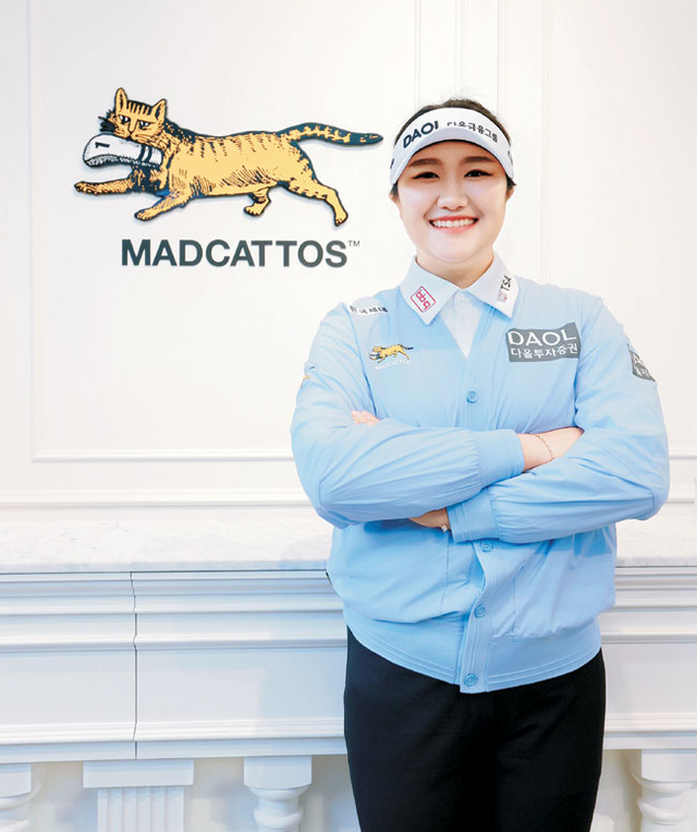 올해 자신의 첫 메이저대회 우승을 노리는 유해란이 지난 6일 자신의 새로운 의류 스폰서의 상징을 배경으로 포즈를 취하고 있다. 매드캐토스 제공