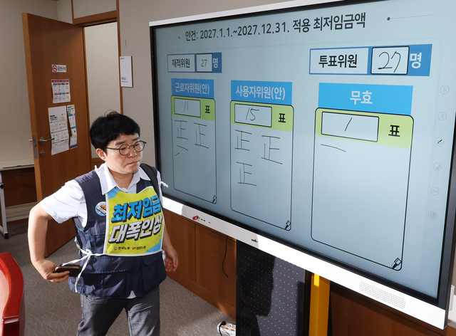 14일 정부세종청사에서 14차 최저임금위원회 전원회의가 끝난 직후 최임위 근로자 위원이 최저임금 표결판 앞으로 지나가고 있다. 뉴시스