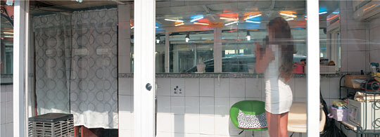 30일 오전 서울 동대문구 ‘청량리 588’로 불리는 집창촌에서 한 성매매 여성이 손님을 맞이하기 위해 안을 볼 수 있도록 설계된 유리방 안에 서 있다.