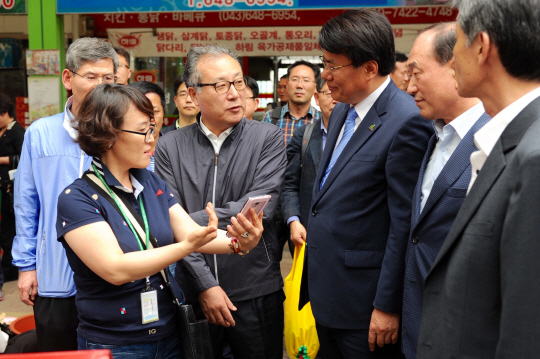 15일 충북 제천시 역전한마음시장을 방문한 한정화(왼쪽 두 번째) 중소기업청장이 이근규(〃 세 번째) 제천시장과 휴대전화의 전통시장 모바일 앱에 대해 이야기하고 있다.