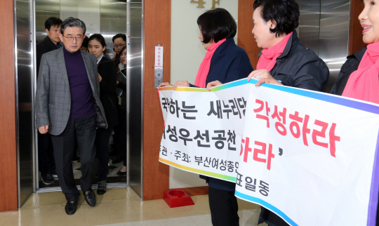 이한구(왼쪽 엘리베이터 앞) 새누리당 공직선거후보자추천관리위원장이 13일 기자실에서 공천 결과를 발표하기 위해 ‘여성우선공천 실시하라’는 플래카드를 들고 있는 부산여성총연대 상임대표들 앞을 지나고 있다. 연합뉴스