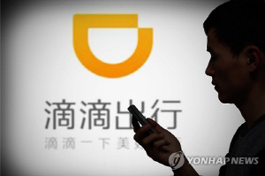 중국 산둥성 지난시에서 한 남성이 디디추싱의 대형 로고 앞에서 휴대전화를 보고 있다.