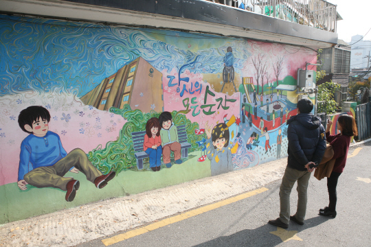 지난 15일 서울 강동구 ‘강풀만화거리’에서 방문객들이 벽에 그려진 웹툰 ‘당신의 모든 순간’의 한 장면을 감상하고 있다.