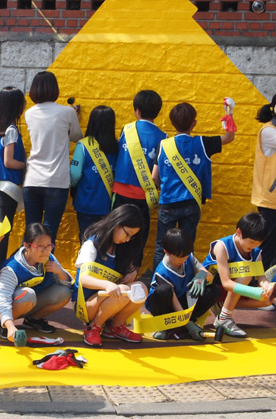 초록우산어린이재단과 국제아동인권센터가 안전한 마을 조성을 위해 진행하고 있는 ‘옐로카펫’ 설치 캠페인에서 경기 수원시 정자초등학교 학생들이 건널목 앞에서 옐로카펫을 설치하고 있다. 초록우산어린이재단 제공