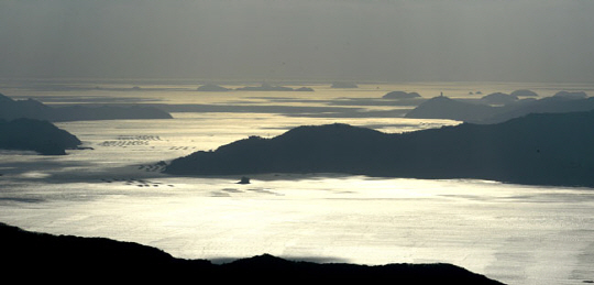오후의 햇살이 기울 무렵 완도 상황봉 정상의 턱밑에서 내려다본 해남 쪽의 바다 풍경. 노란 봄볕으로 가득한 바다 너머로 해남의 땅끝마을이 보인다.