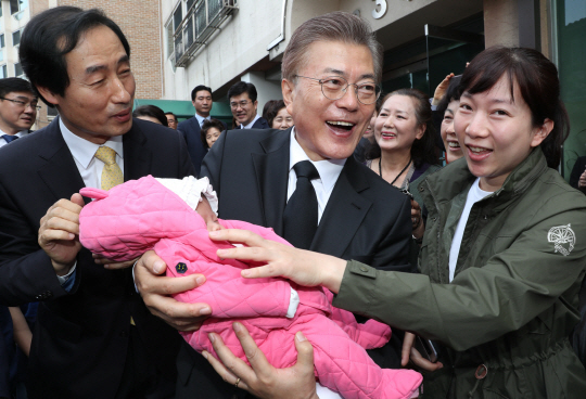 문재인 대통령이 10일 오전 서울 서대문구 홍은동 자택을 나서면서 생후 1개월 된 이웃 주민의 아이를 두 팔로 감싸 안고 밝게 웃고 있다.