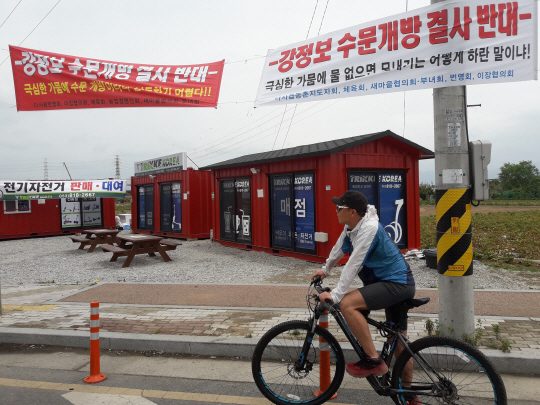 지난 7일 오후 대구 달성군 다사읍 강정고령보 인근 도로변에 걸려 있는 보 개방반대 현수막 앞을 자전거를 탄 한 주민이 지나가고 있다.   박천학 기자