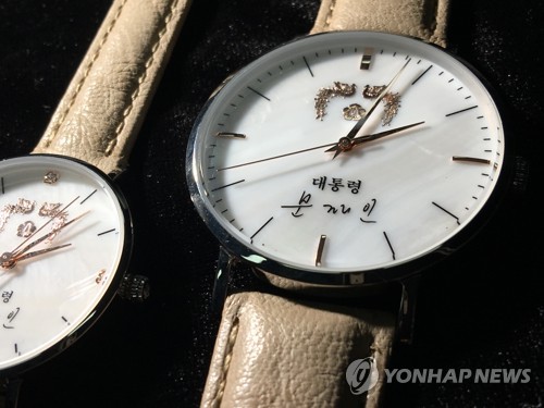 (서울=연합뉴스) 문재인 대통령의 이름이 새겨진 손목시계가 나왔다. 이 시계는 뒷면에 ‘사람이 먼저다’란 글귀가 쓰여 있고 시계 앞면에는 봉황 마크와 ‘대통령 문재인’이라고 쓰여 있다. 남성용과 여성용.