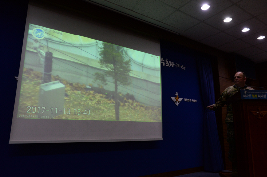 채드 캐럴(육군 대령) 유엔군사령부 공보실장이 22일 서울 용산 국방부 브리핑실에서 지난 13일 북한 병사가 판문점 공동경비구역(JSA)을 통해 귀순할 당시 상황이 담긴 CCTV 영상을 공개하고 있다. 스크린에 떠 있는 영상에는 북한 추격군에게 총격을 당한 북한 병사가 벽 아래 낙엽 더미 위에 쓰러져 있다.