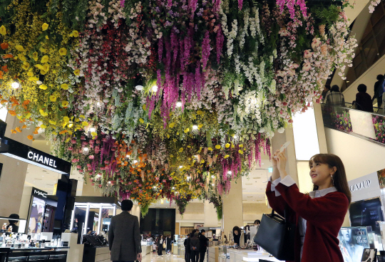 서울 중구 소공로에 위치한 신세계백화점 본점이 꽃으로 장식을 한 가운데 6일 1층 꽃 장식 앞에서 모델이 휴대전화 카메라에 이를 담는 포즈를 취하고 있다.   신세계백화점 제공