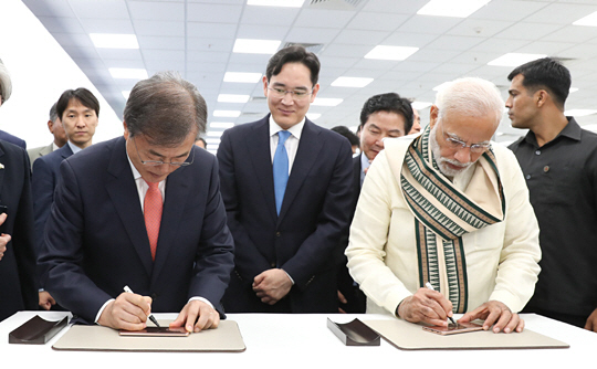 문재인 대통령이 9일 나렌드라 모디(오른쪽) 인도 총리와 함께 인도 뉴델리 인근 노이다 공단에서 열린 삼성전자 제2공장 준공식에 참석, 이재용(가운데) 삼성전자 부회장이 지켜보는 가운데 신규 라인에서 생산된 휴대전화에 서명하고 있다.  뉴시스