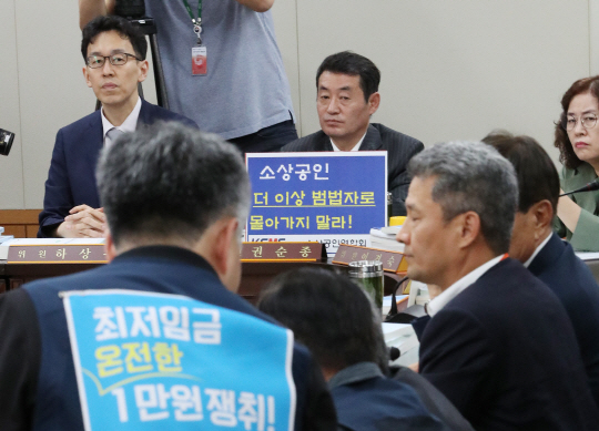 권순종(뒷줄 오른쪽) 소상공인연합회 부회장이 10일 정부세종청사에서 열린 최저임금위원회 전원회의에서 ‘소상공인 더 이상 범법자로 몰아가지 말라’는 팻말을 책상 위에 두고 앉아 있다. 연합뉴스