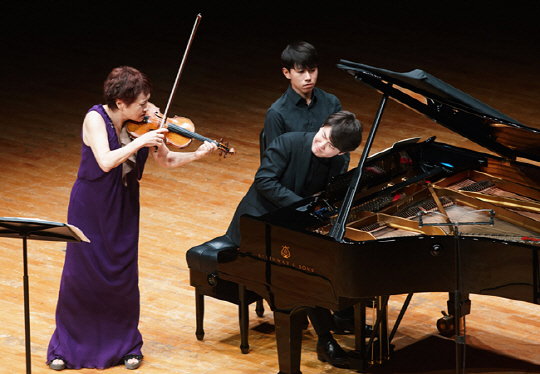 12일 서울 예술의전당에서 열린 콘서트에서 정경화(왼쪽)와 조성진이 서로를 마주 보며 연주하고 있다. 뒤쪽은 악보를 넘겨 주는 페이지 터너.   예술의전당 제공