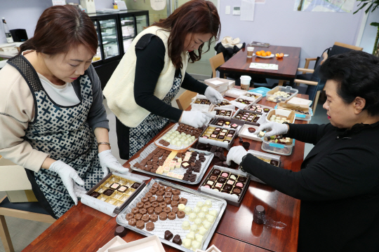 성수지앵 협동조합 조합원들이 직접 만든 수제화 모양을 본뜬 초콜릿을 판매하기 위해 상자에 담아 포장하는 모습.  성동구청 제공