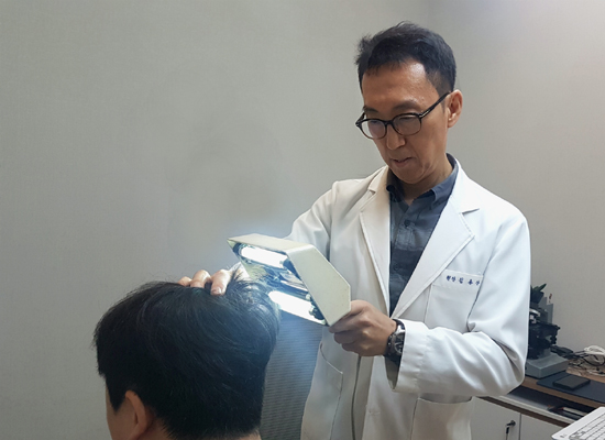 김용상 계피부과의원 원장이 탈모환자의 머리숱 상태를 점검하고 있다.