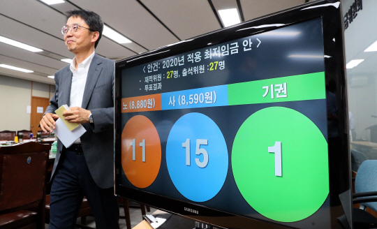 박준식 최저임금위원회 위원장이 12일 오전 5시 30분쯤 정부세종청사에서 열린 13차 전원회의에서 13시간의 마라톤 심의 끝에 2020년 최저임금을 2.9% 인상한 8590원으로 확정하는 방안이 15명의 동의(미동의 11, 기권1)로 통과된 직후 투표 결과가 표시된 화면 앞을 미소를 지으면서 지나가고 있다.  뉴시스