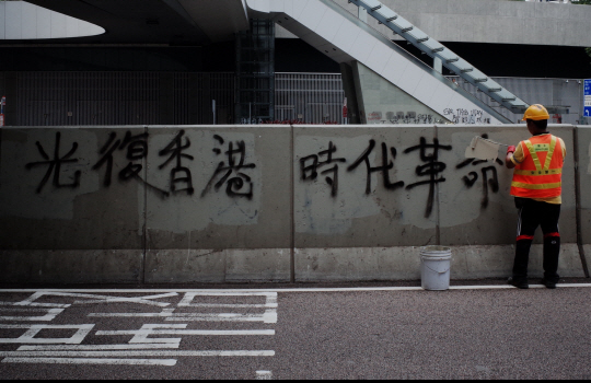 19일 홍콩 애드미럴티 지역 정부청사 앞에서 한 환경미화원이 전날 열린 도심 집회 시위 참가자가 도로 난간에 한 낙서를 지우고 있다.  연합뉴스