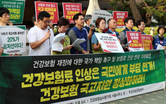 무상의료운동본부 관계자가 22일 오후 서울 서초구 효령로 건강보험심사평가원 서울사무소 앞에서 열린 ‘건강보험 재정에 대한 국가 책임 촉구 및 보험료 인상 반대 기자회견’에서 “건강보험 국고지원을 정상화하라”며 정부를 규탄하고 있다.  연합뉴스