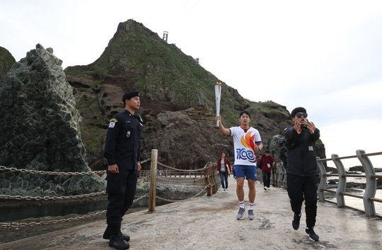 26일 오전 독도경비대 헬기장에서 열린 제100회 전국체전 성화 채화 행사에서 오요셉(가운데) 독도경비대원이 성화를 선착장으로 봉송하고 있다.  연합뉴스