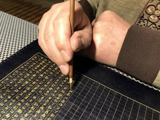 현담 허락 작가가 아교풀에 갠 금가루(金粉)를 가는 붓(細筆)으로 찍어 한지 위에 화엄경을 필사하고 있다. 모두 12틀 병풍 중 세 번째 병풍을 위한 금사경 작업이다. 고려사경문화원 제공