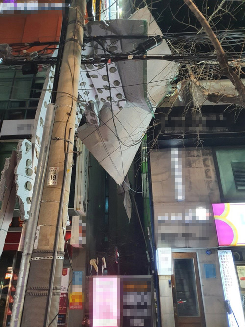 8일 오전 부산 부산진구 서면시장 인근 상가 건물 외벽에 부착됐던 대형 단열재가 강풍에 떨어져 전신주와 전선 사이에 위태롭게 걸려 있다. 부산경찰청 제공