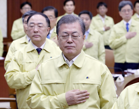 문재인 대통령이 30일 오전 서울 종로구 세종대로 정부서울청사에서 홍남기(왼쪽) 부총리 겸 기획재정부 장관 등이 참석한 가운데 열린 신종 코로나바이러스 감염증 대응 종합점검회의에서 국기에 대한 경례를 하고 있다.  연합뉴스