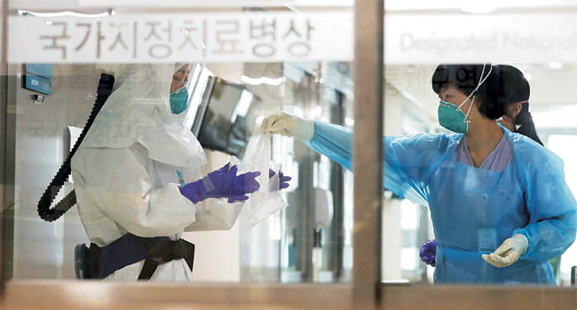 26일 오전 신종 코로나바이러스 감염증 확진자가 1146명을 기록해 사회 전체가 대혼란 속으로 빠져드는 상황에서도 생명을 지키려는 의료진의 사투가 전국 곳곳에서 이어지고 있다. 사진은 국가지정치료병상으로 지정된 울산대병원 의료진이 25일 환자들을 돌보기 위해 방호복을 착용하는 모습.  연합뉴스