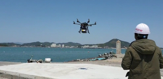 전남도 용역 연구를 수행하는 한 드론 조종사가 4월 초 고흥군 도양읍 상화도 선착장에서 물건을 실은 드론이 착륙하는 모습을 지켜보고 있다. 이 드론은 2.1㎞ 떨어진 도양읍 녹동 신항에서 날아왔다가 ‘자동 왕복 비행’ 방식으로 되돌아갔다. 왼쪽 아래 사진은 전남도가 제작한 물건 배달용 드론. 전남도청 제공