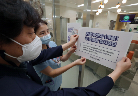 22일 오전 세종시에 있는 대형병원 직원들이 질병관리청의 인플루엔자(독감) 백신 무료접종 일시중단 결정에 따라 접종 중단 안내문을 출입구에 붙이고 있다.  연합뉴스