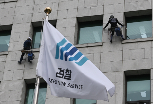 검찰이 ‘옵티머스 사건’에 수사팀 규모를 2배 이상 늘리는 등 의혹 수사를 확대하는 가운데 14일 오전 서울 서초구 대검찰청에서 검찰기 너머로 청소업체 직원들이 외벽 유리를 청소하고 있다.
