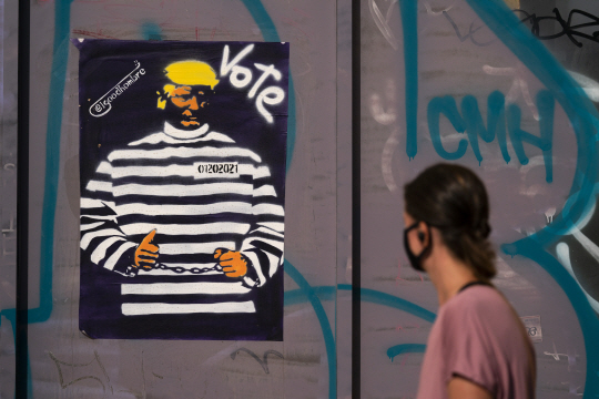 미국 대통령 선거를 하루 앞둔 2일 캘리포니아주 로스앤젤레스에서 한 여성이 도널드 트럼프 대통령을 수갑이 채워진 모습으로 희화화한 포스터 앞을 지나가고 있다. AP뉴시스