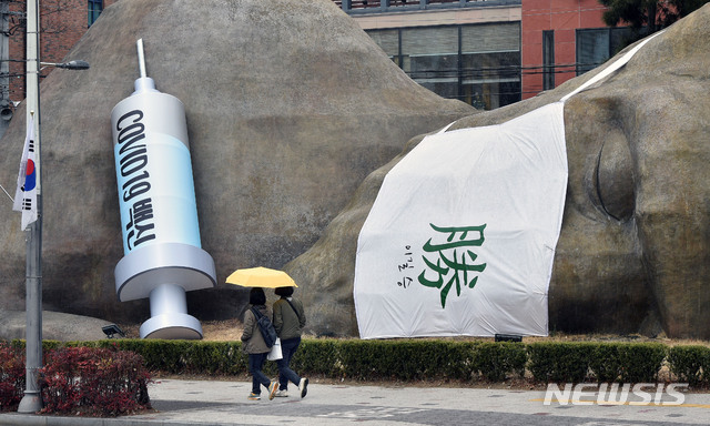 [대구=뉴시스] 신종 코로나바이러스 감염증(코로나19) 백신 국내 접종 시작을 하루 앞둔 25일 오후 대구 달서구 진천동 선사유적공원 입구 원시인 조형물에 대형 주사기가 설치돼 눈길을 끌고 있다. 2021.02.25.