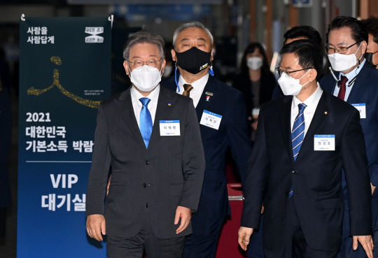 이재명(왼쪽) 경기지사가 28일 오전 경기 고양시 킨텍스에서 개막한 ‘2021 대한민국 기본소득 박람회’에 참석하기 위해 관계자들과 함께 개막식장으로 들어서고 있다.