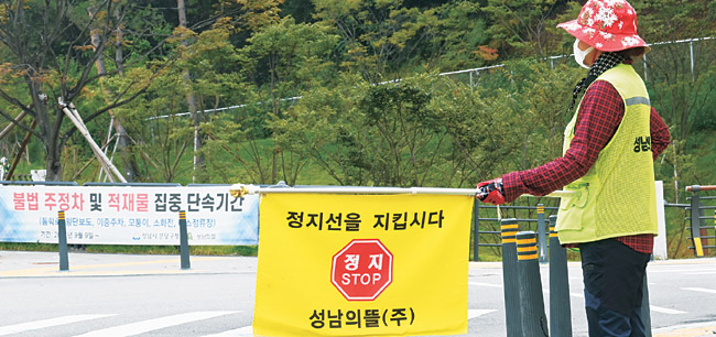 30일 오전 경기 성남시 대장동 일대에서 대장동 개발 시행사인 ‘성남의뜰’ 조끼를 입은 한 관계자가 횡단보도 앞에서 차량 정지선 준수 교통신호 깃발을 들고 있다. 특혜 의혹에 휩싸인 대장동 개발사업을 경고하듯 ‘정지(stop)’라는 글자가 선명하게 들어온다.  김선규 기자