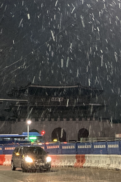 10일 새벽어둠이 가시지 않은 광화문 거리에 자동차 헤드라이트와 가로등 불빛에 비쳐 하얗게 빛나는 올해 첫눈이 흩날리고 있다.  연합뉴스