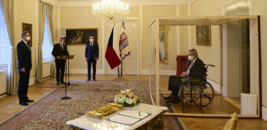 코로나19 확진 판정을 받은 밀로시 제만(오른쪽) 체코 대통령이 28일 수도 프라하 외곽 라니에 위치한 대통령 관저에서 투명 플라스틱 패널 속에 격리된 채 휠체어에 앉아 페트르 피알라(왼쪽) 신임 총리로부터 취임 선서를 받고 있다. 77세 고령인 제만 대통령은 확진된 뒤 병원에 이틀간 입원했다가 27일 퇴원했다.  EPA 연합뉴스