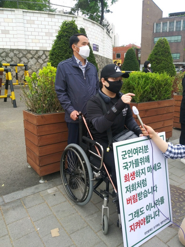 천안함 폭침 마지막 구조자로 가장 심한 부상을 당해 치료 중인 신은총 예비역 하사가 최원일 전 천안함 함장이 미는 휠체어에 탄 채 2021년 4월23일 서울 용산 국방부 정문 앞에서 천안함 46용사와 생존자, 유족들 명예회복을 위한 정부의 대책을 촉구하는 1인시위를 하고 있다. 천안함 생존자 예비역전우회 제공