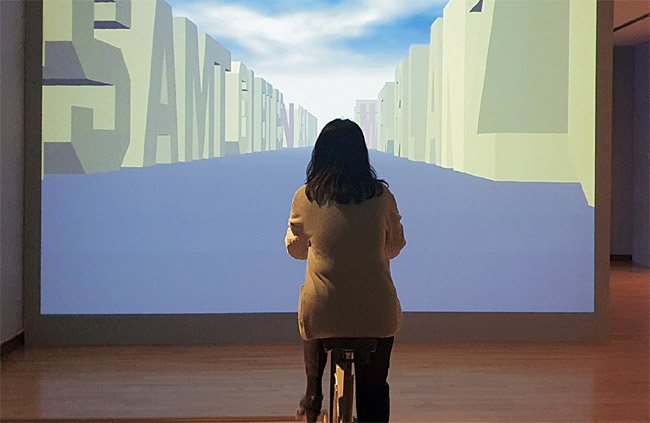 독일 작가 제프리 쇼의 1988년 작 ‘읽을 수 있는 도시’. 김희랑 광주시립미술관 학예실장이 실내 자전거 페달을 돌려서 스크린 속 도시의 ‘글자 빌딩’을 움직이는 시범을 보이고 있다.