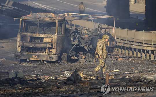 (키예프 AP=연합뉴스) 26일(현지시간) 우크라이나 키예프 거리에서 불탄 군용 트럭 잔해 앞으로 우크라이나군인이 지나고 있다. 2022.2.26