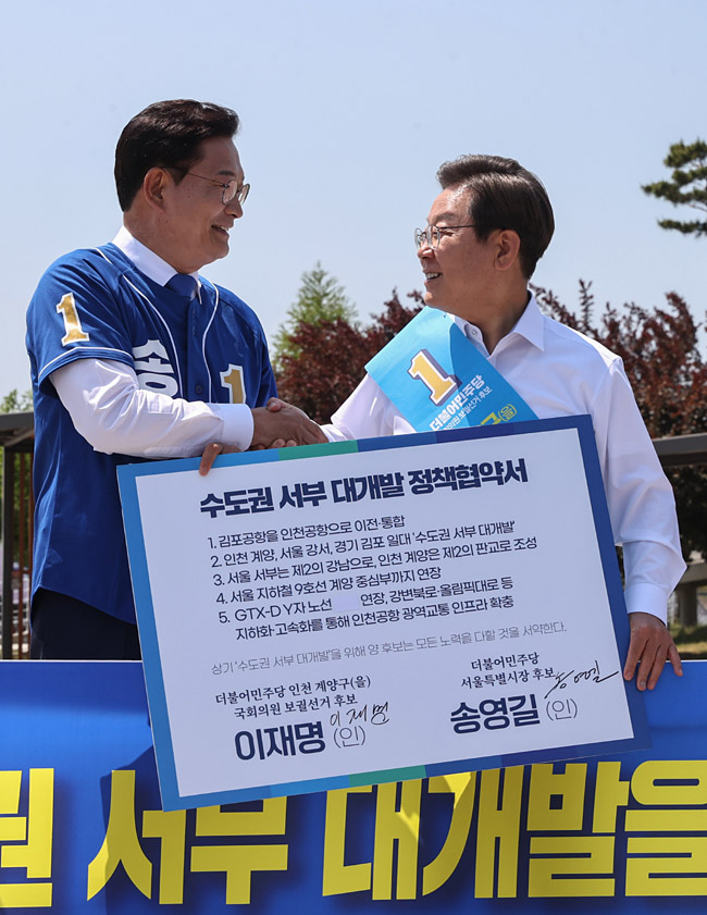 더불어민주당 송영길(왼쪽) 서울시장 후보와 이재명 인천 계양을 국회의원 보궐선거 후보가 지난 27일 김포시 고촌읍 아라 김포여객터미널 아라마린센터 앞 수변 광장에서 열린 김포공항 이전 수도권 서부 대개발 정책협약 기자회견에서 협약서에 서명한 뒤 악수하고 있다. 뉴시스