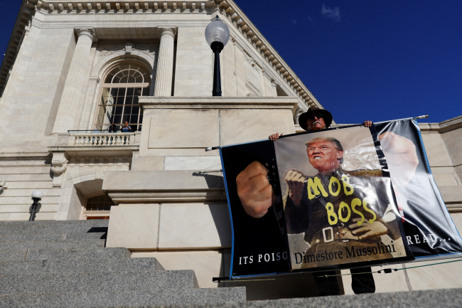 미국 하원에서 지난해 1·6 의회의사당 난입 사건에 대한 첫 공개 청문회가 열린 9일 한 시위자가 워싱턴DC 의회의사당 앞에서 도널드 트럼프 전 대통령의 사진 위에 ‘폭동 두목’이라고 적은 플래카드를 들고 시위하고 있다.  로이터 연합뉴스