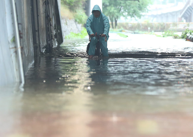 30일 오전 침수된 서울 은평구 불광천에서 시민이 물에 반쯤 잠긴 자전거를 타고 이동하고 있다. 뉴시스