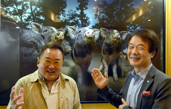 건축과 디자인의 협업을 추진 중인 김종훈(오른쪽) 한미글로벌 회장과 김영세 이노디자인 회장이 지난 14일 서울 강남구 한미글로벌 본사에서 만나 환하게 웃고 있다. 뒷배경은 사진작가로 활동하고 있는 김종훈 회장의 지인인 박찬원 씨의 작품 ‘돼지가 우리를 본다’. 밤하늘을 보고 있는 어린 돼지들과 돼지꿈의 소망을 담았다.  김선규 기자