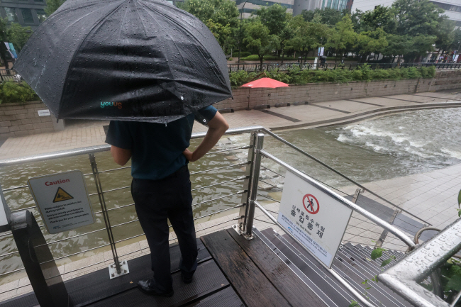 3일 오전 한 경찰관이 밤부터 쏟아진 폭우로 수위가 올라가 출입이 통제된 서울 중구 청계천을 순찰하며 바라보고 있다. 연합뉴스
